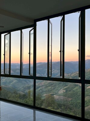 Quarto com grandes janelas do chão ao teto, com vista para uma paisagem montanhosa.
