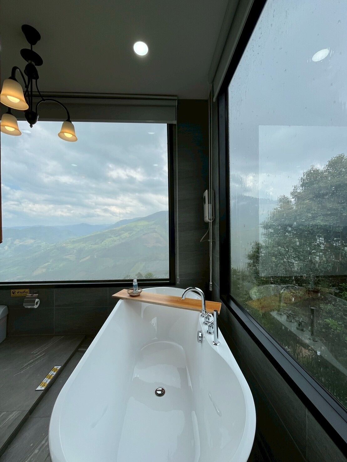 Um banheiro moderno com uma banheira grande, uma prateleira de madeira e vista para uma paisagem montanhosa.