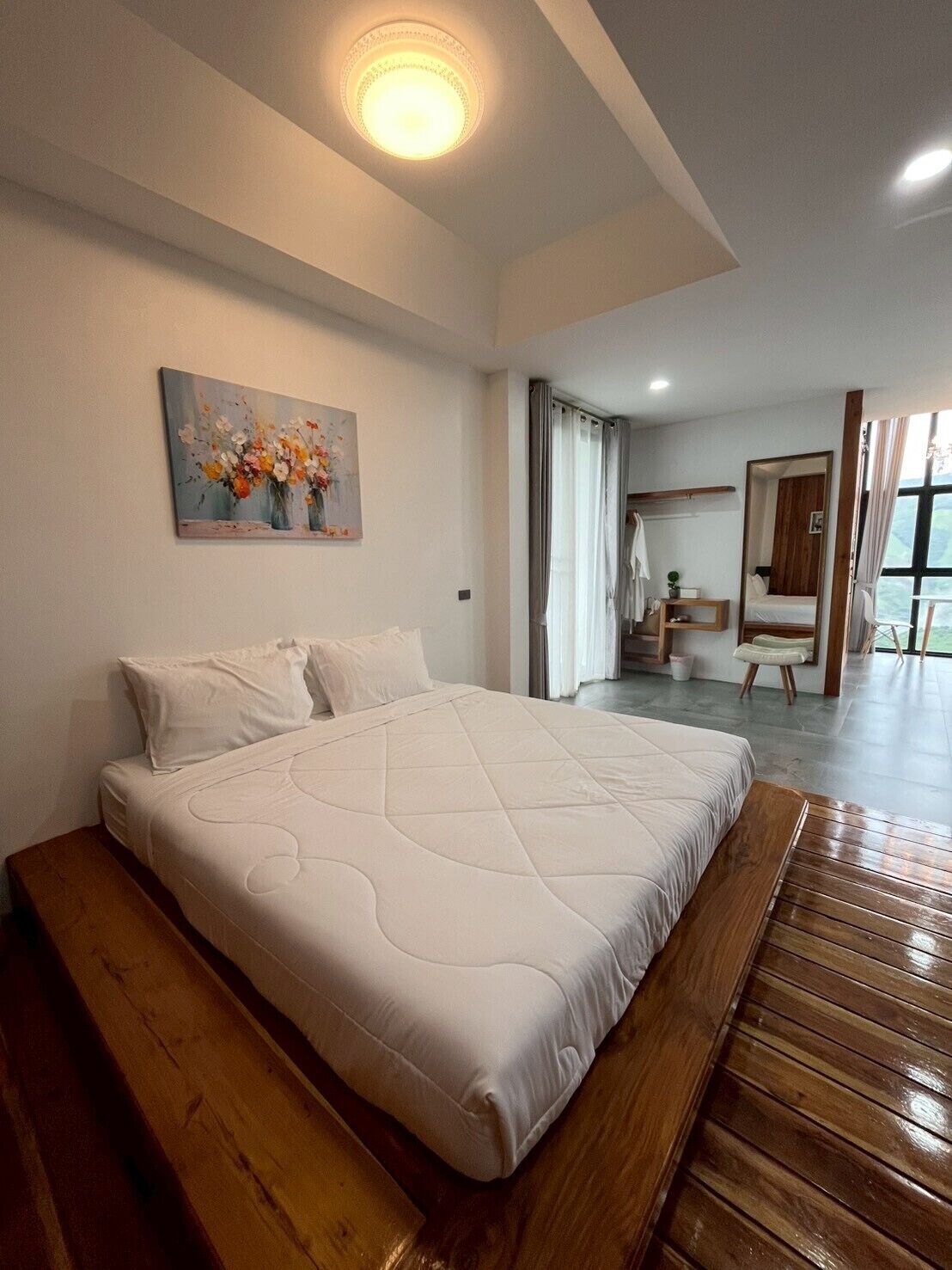 Un dormitorio con una cama grande, un cuadro en la pared, un banco de madera y vistas a un balcón.