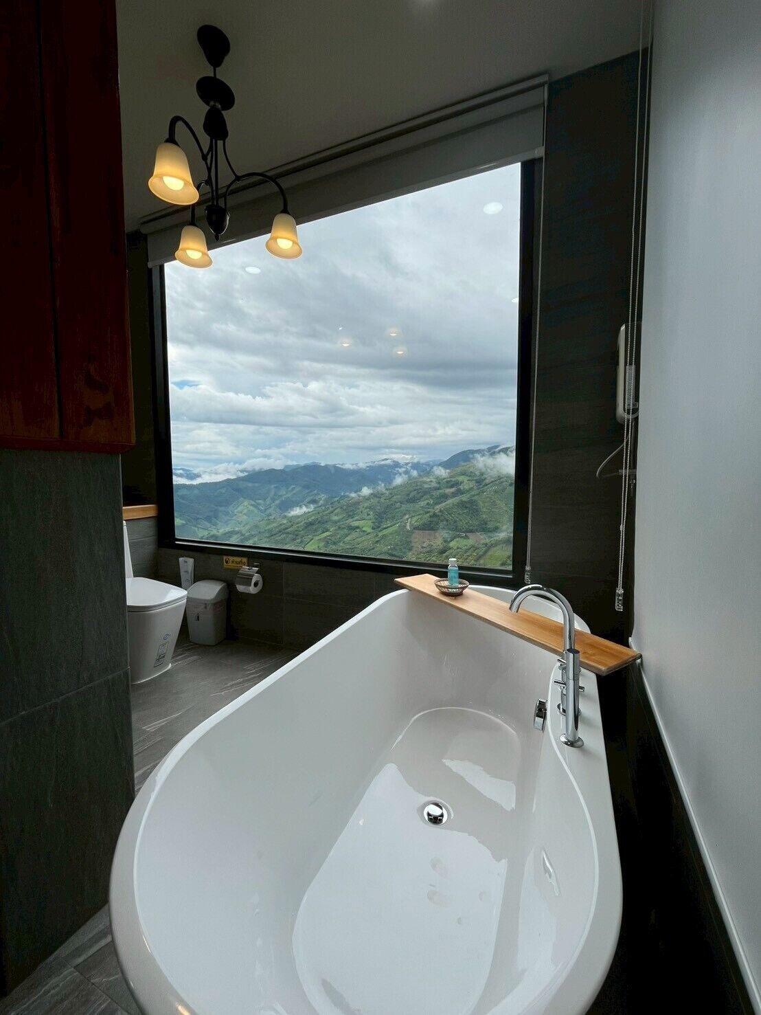 Un baño moderno con una bañera grande, una ventana con vistas a montañas y una lámpara en el techo.