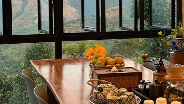 A dining area with a table set for tea, a view of a mountainous landscape, and a large window with multiple panes. - Mei Nai Home (Pua)