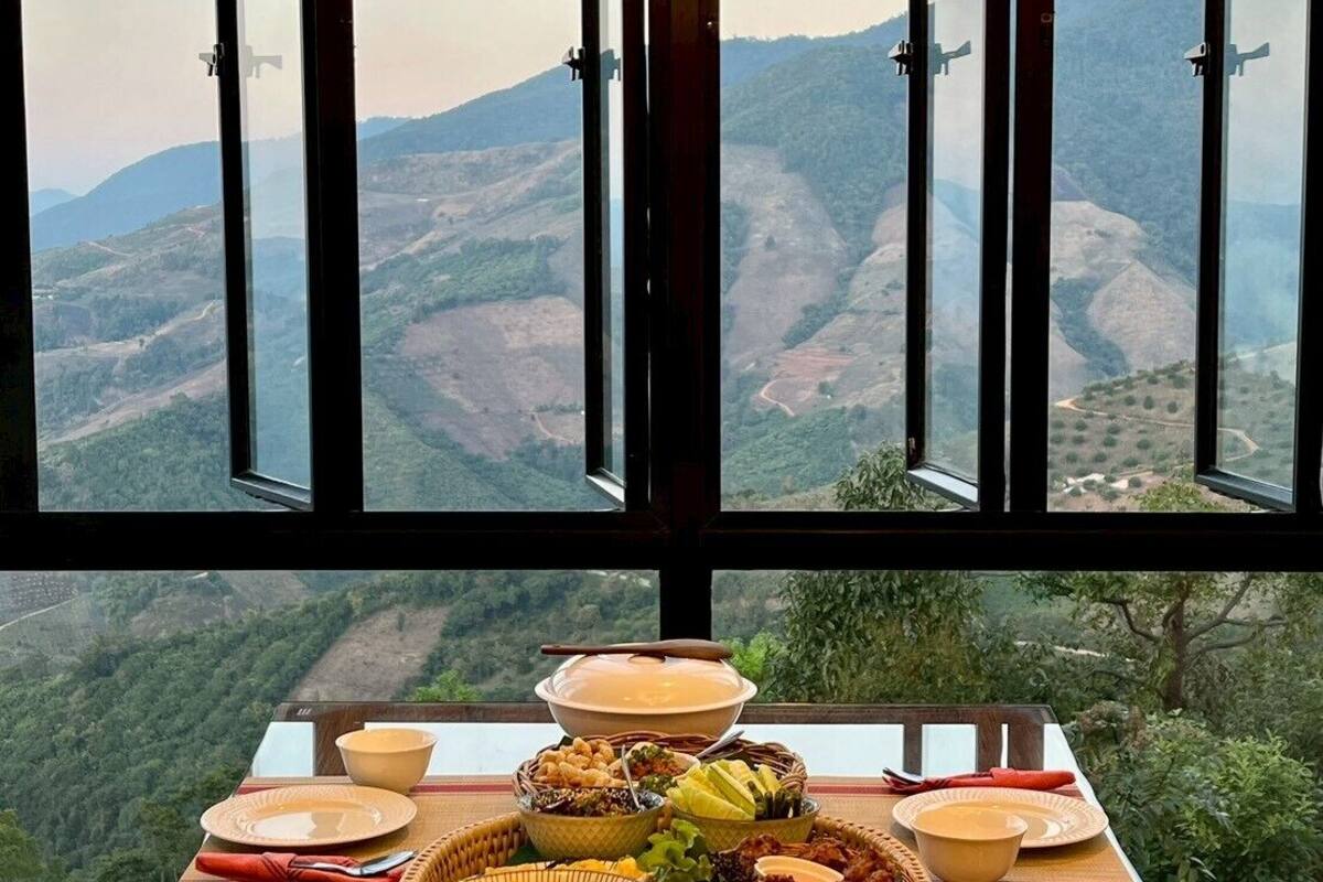 Una mesa de comedor dispuesta con diversos platos y una vista panorámica de montañas a través de grandes ventanales.