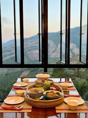 A dining table set with various dishes and a scenic mountain view through large windows.