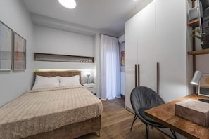Ein Schlafzimmer mit Bett, Nachttisch, Lampe und Schreibtisch mit Stuhl.
