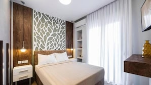 Ein Hotelzimmer mit einem Bett, Nachttischen, einem Kleiderschrank, einer eingebauten Regaleinheit und einem großen Fenster mit Vorhängen.