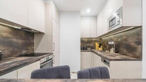 A modern kitchen with a built-in microwave, a stove, and a sink. There are two grey chairs at the dining table.