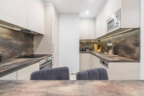 A modern kitchen with a built-in microwave, a stove, and a sink. There are two grey chairs at the dining table.