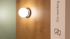 A wooden wall with a circular light fixture and a vertical sign with the text 'Co-working.'