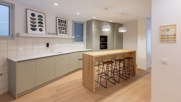 A modern kitchen with a central island, bar stools, and a window.