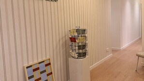 A hallway with a striped wall, a framed artwork, a display of postcards, and a hanging light fixture.