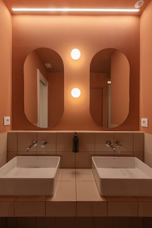 Een badkamer met twee wasbakken, een grote spiegel en een wandlamp.