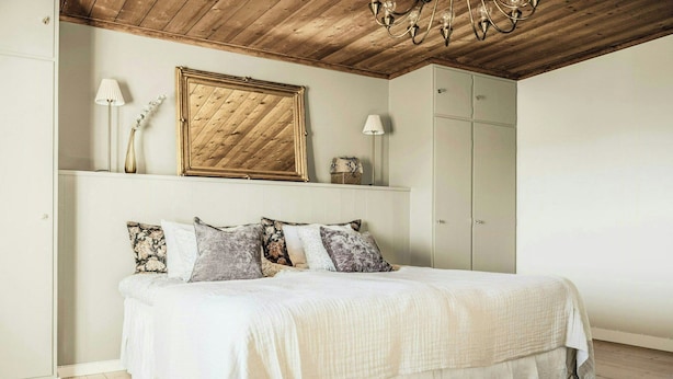 Ein Schlafzimmer mit Bett, Holzboden, einer Chandelüster, einem gerahmten Spiegel und einem Kleiderschrank.