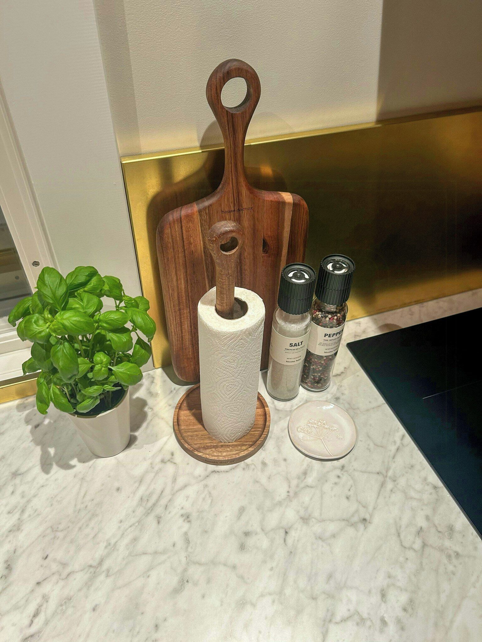 A kitchen counter with a wooden cutting board, a roll of paper towels, salt and pepper shakers, a small potted plant, and a decorative plate.