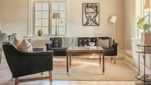 Ein Wohnzimmer mit Holzbalkendecke, einem schwarzen Sofa, einem Couchtisch und einer Lampe.