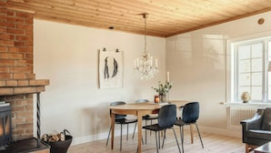 Ein Essbereich mit Kamin aus Backstein, Holzbalkendecke, einer Chandelier und einem Tisch mit Stühlen.