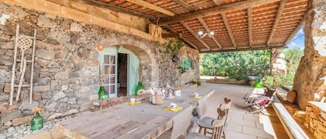 Un área de comedor al aire libre rústica, con pared de piedra, mesa y sillas de madera.