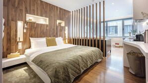 A modern hotel room with a wooden accent wall, a large bed, a desk, and a view of the city. - Modern Studio in Central Psyri King Bed (Athina)