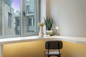 Un rincón de una habitación con una ventana, una silla y una mesita con una planta y una lámpara.