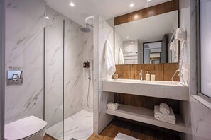 Un baño moderno con ducha de mampara de vidrio, tocador de madera y un espejo grande.
