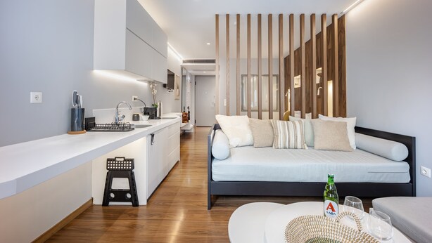 A modern kitchen with a built-in island, a dining area with a round table, and a bedroom with a bed and bedside tables. - Modern Studio in Central Psyri King Bed (Athina)