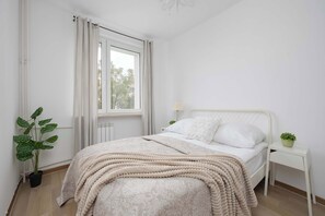 Ein Schlafzimmer mit einem Bett, einem Nachttisch mit Pflanze, einem Fenster mit Vorhängen und einer Heizung.