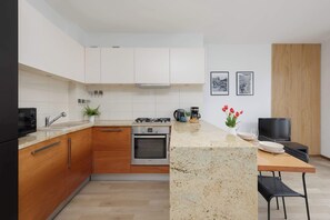 Eine moderne Küche mit weißen Schränken, einem Einbauofen, einer Arbeitsplatte aus Granit und einem Essbereich mit Fernseher und Holzpaneele.