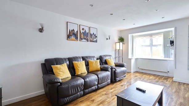 A modern living room with a leather sofa, wooden flooring, a coffee table, and a window with natural light. - Host Stay - Urban Nest LIV (Liverpool)