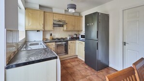 A compact kitchen with wooden cabinets, a stainless steel refrigerator, a gas stove, and a microwave. - Host Stay - Urban Nest LIV (Liverpool)