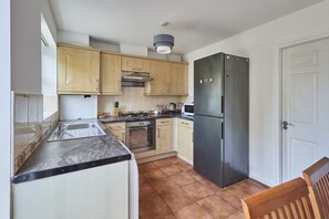A compact kitchen with wooden cabinets, a stainless steel refrigerator, a gas stove, and a microwave. - Host Stay - Urban Nest LIV (Liverpool)