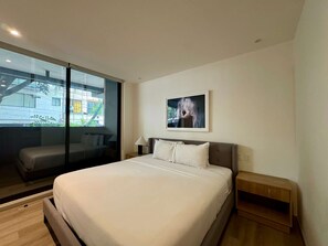 Ein modernes Hotelzimmer mit einem großen Bett, einem Nachttisch, einem Fenster mit Blick auf Gebäude und einem gerahmten Bild an der Wand.