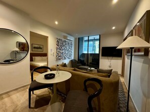 Ein modernes Wohnzimmer mit einer Couch, Sesseln, einem kleinen Tisch, einem Fernseher und einem großen Fenster.