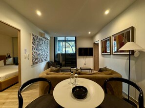 Ein modernes Hotelzimmer mit einer Couch, einem Esstisch mit Stühlen, einem Fernseher und Kunstwerken an den Wänden.