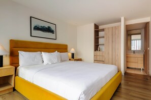Ein Hotelzimmer mit einem großen Bett, Nachttischen, einem Kleiderschrank und einem durch eine offene Tür einsehbaren Badezimmer.
