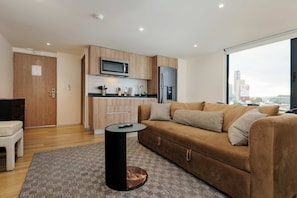 A modern living room with a sofa, a coffee table, a TV, and a kitchen area with a microwave and refrigerator. - w Urban 1BR w/ AC in the Heart of Cuauhtemoc (Mexico City)