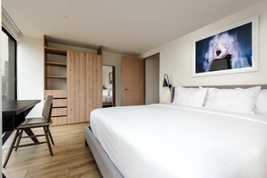 Ein modernes Hotelzimmer mit einem großen Bett, einem Schreibtisch mit Stuhl, einem Kleiderschrank und einem Bild an der Wand.