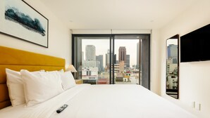 Ein Hotelzimmer mit Bett, Blick auf die Stadt, Fernseher und einem Gemälde an der Wand.