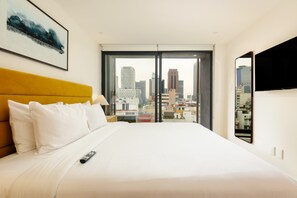 Ein Hotelzimmer mit Bett, Blick auf die Stadt, Fernseher und einem Gemälde an der Wand.