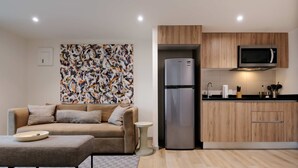 Ein modernes Wohnzimmer mit Sofa, Couchtisch, Kühlschrank und Küchenzeile mit Holzschränken und einer Mikrowelle.