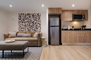 Ein modernes Wohnzimmer mit Sofa, Couchtisch, Kühlschrank und Küchenzeile mit Holzschränken und einer Mikrowelle.