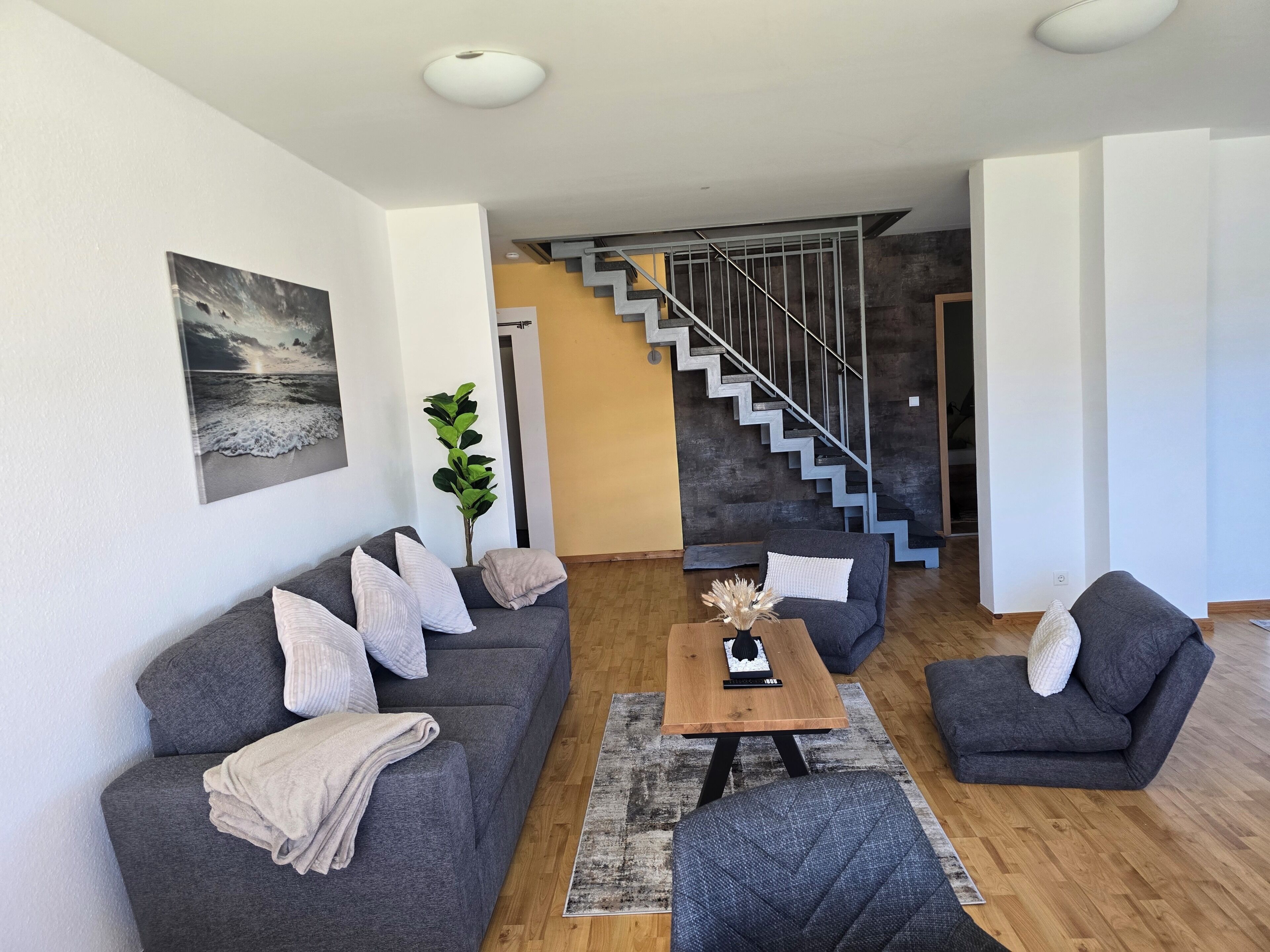 Una sala de estar moderna con un sofá gris, una mesa de centro y una escalera que conduce a otro nivel.