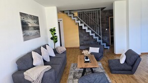 Ett modernt vardagsrum med en grå soffa, ett soffbord och en trappa som leder upp till ett annat plan.
