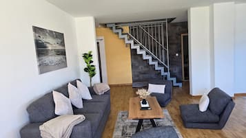 Una sala de estar moderna con un sofá gris, una mesa de centro y una escalera que conduce a otro nivel.