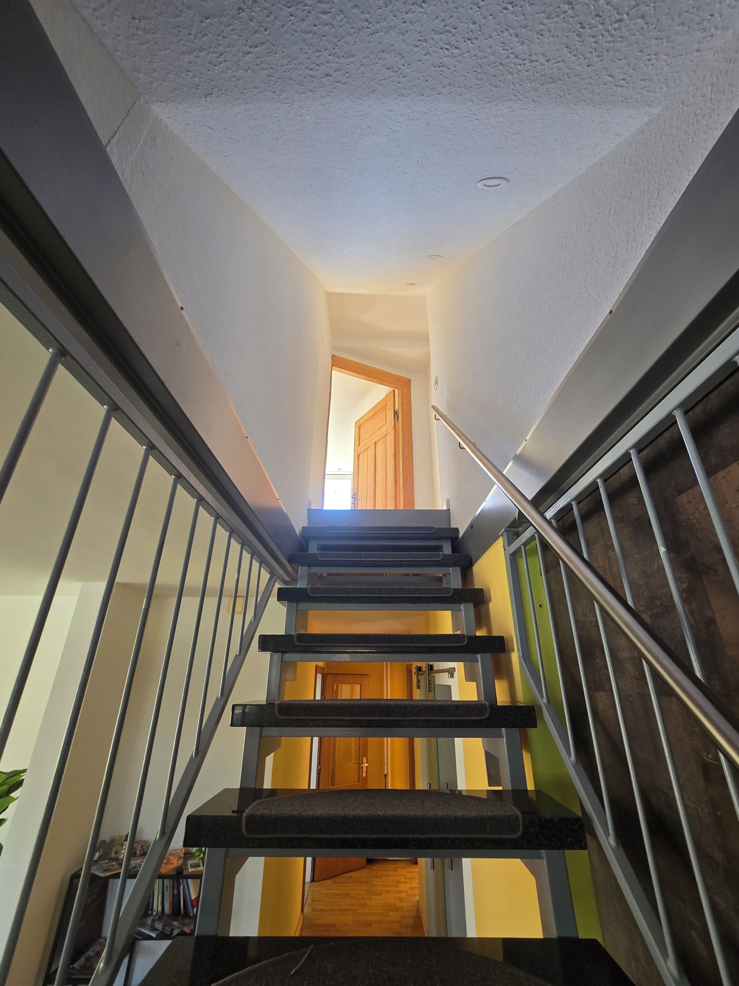A staircase with metal railings, a wooden door at the top, and a view into a room with a wooden floor.