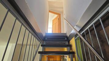 A staircase with metal railings, a wooden door at the top, and a view into a room with a wooden floor.