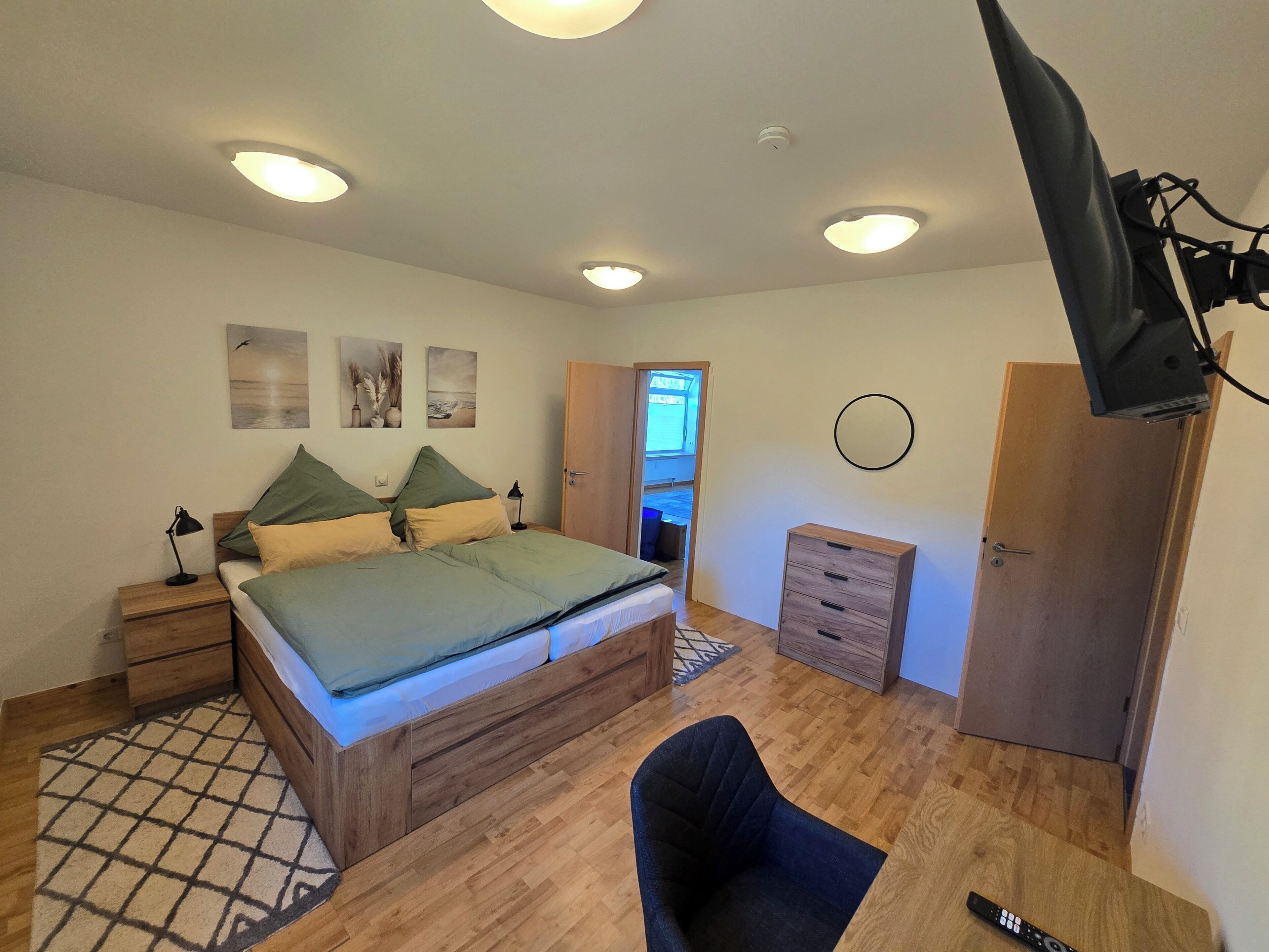 Ein Schlafzimmer mit Bett, Nachttischen, Schreibtisch, Stuhl, Kleiderschrank und Deckenleuchte.