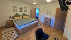 Ett sovrum med en säng, sängbord, ett skrivbord, en stol, en garderob och en taklampa.