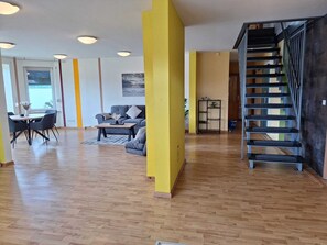 Àmplia zona d'estar amb sòl de fusta, un sofà, una taula de centre i una escala.