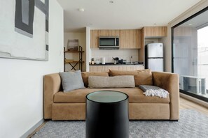 Ein modernes Wohnzimmer mit einer Couch, einem Glastisch und einer Küche im Hintergrund.