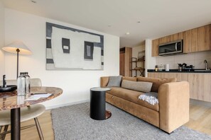 Ein modernes Wohnzimmer mit einer Couch, einem runden Tisch, einer Lampe und einer Küchenzeile im Hintergrund.