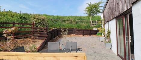 A patio with a wooden table and chairs, a gravel path, and a wooden fence.
